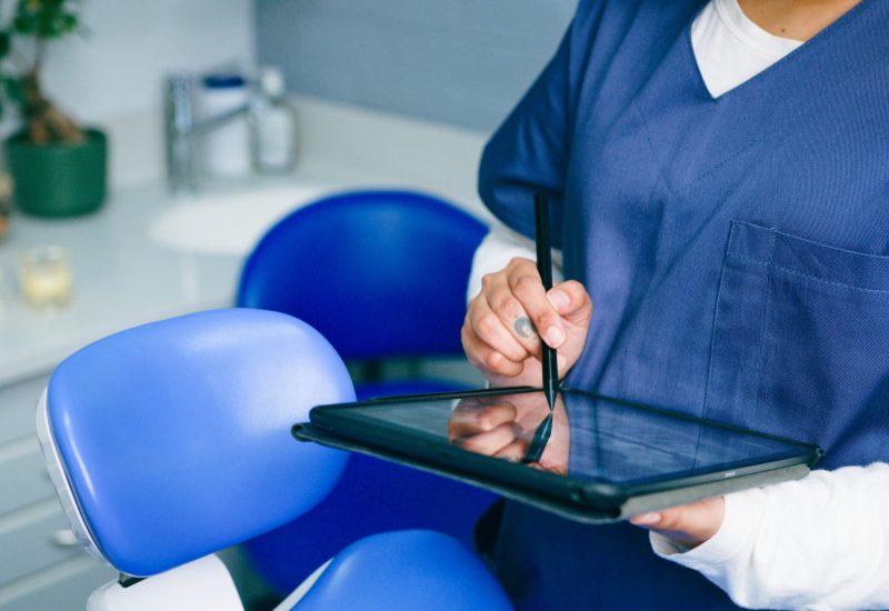 Healthcare Professional Using Tablet in Modern Dental Office A healthcare worker in scrubs utilizes a digital tablet in a contemporary dental office. The image emphasizes modern technology and professionalism in healthcare settings, showcasing efficiency and attention to detail.
