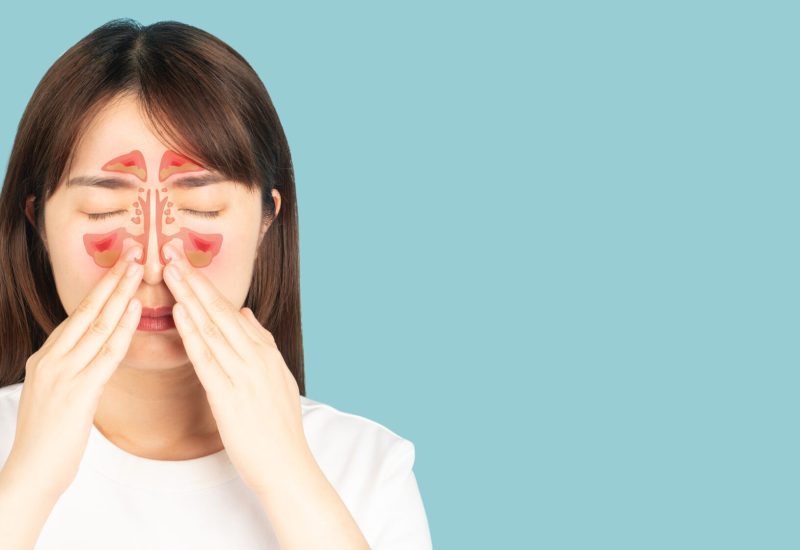 Asian woman suffering from sinusitis with nasal congestion of mucus or pus over blue background. Causes of rhinosinusitis include bacterial infections, viral infections and allergies.